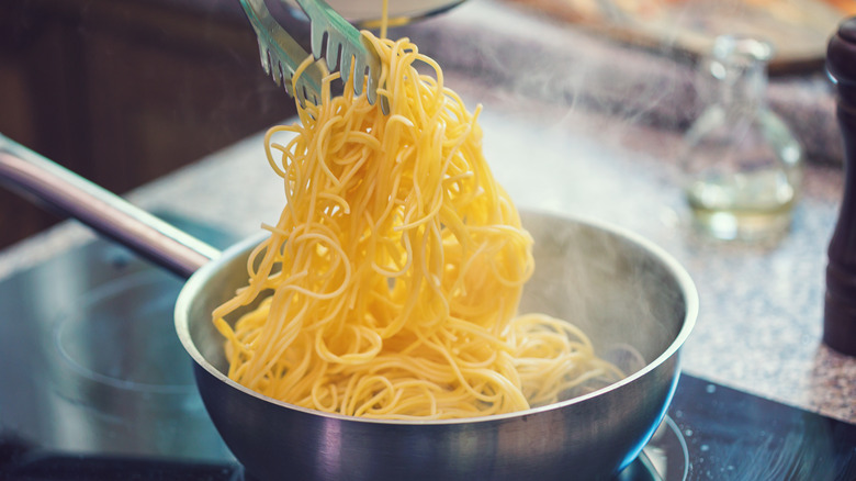 tongs lifting hot pasta from pot