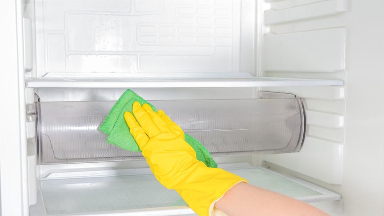 gloved hand scrubbing empty fridge drawer