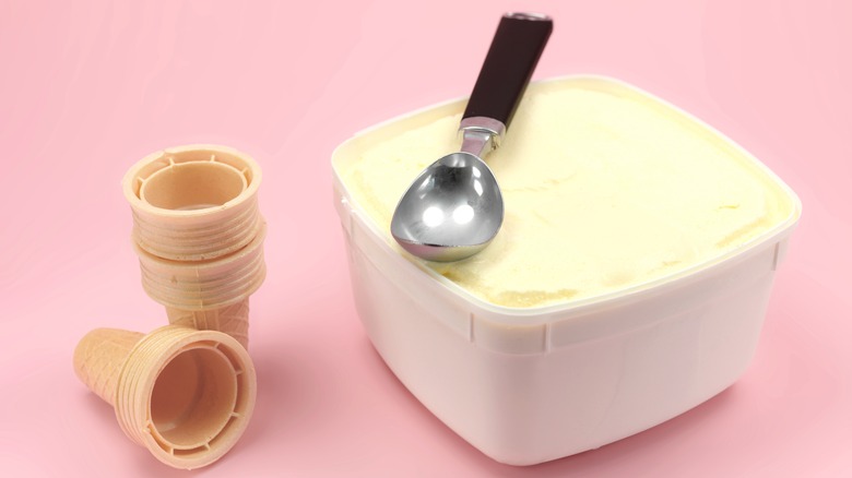 Tub of vanilla ice cream next to sugar cones