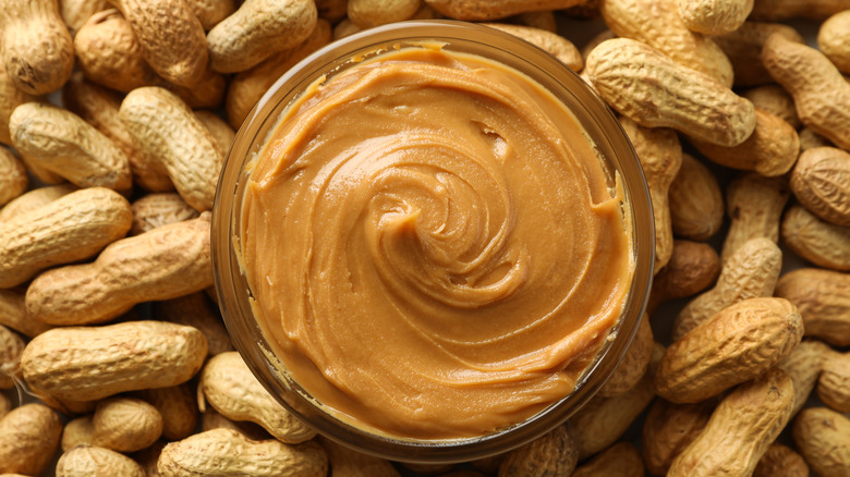 Glass jar of peanut butter on a bed of peanuts 