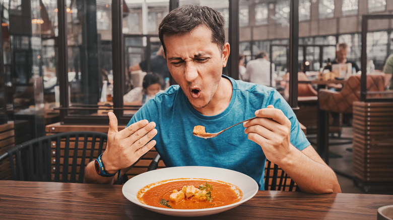 A man winces while eating hot soup