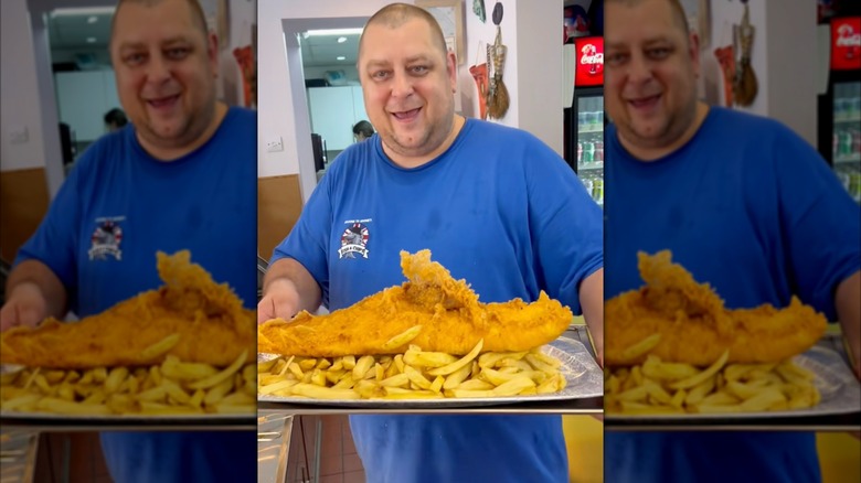 A person in a blue shirt holding a large plate of fish and chips