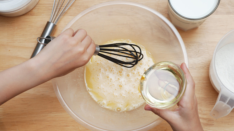 Hands whisking in a clear, plastic mixing bowl