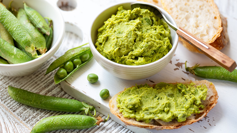 Fresh and mashed peas with bread on table
