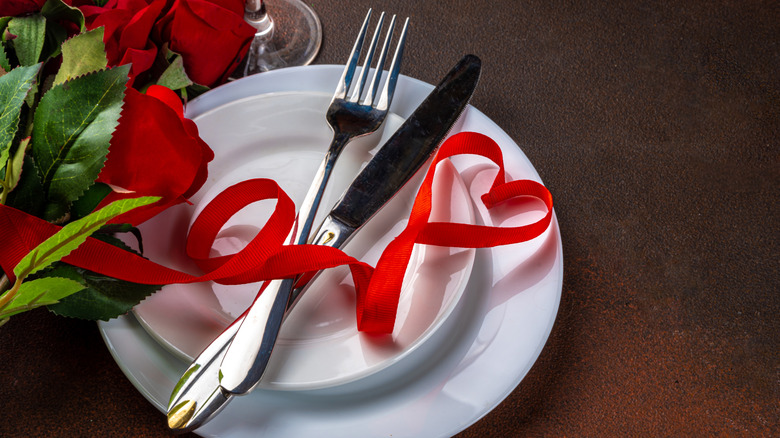 A table setting decorated with red roses and a heart-shaped ribbon