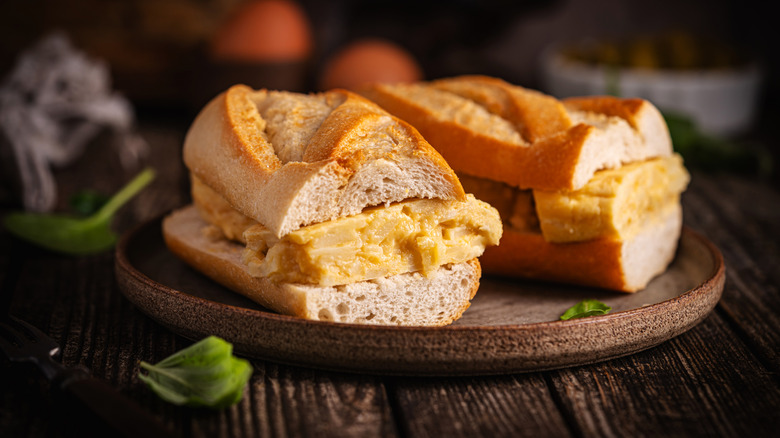 Two halves of a sandwich with Spanish tortilla on a plate on a wooden table