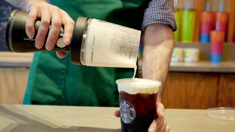 Barista pouring cold foam on coffee