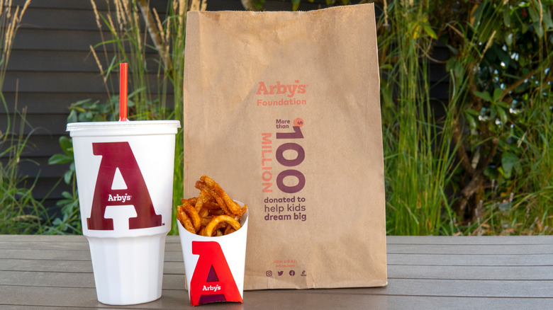 Arby's bag next to a large drink in a plastic cup and a container of curly fries