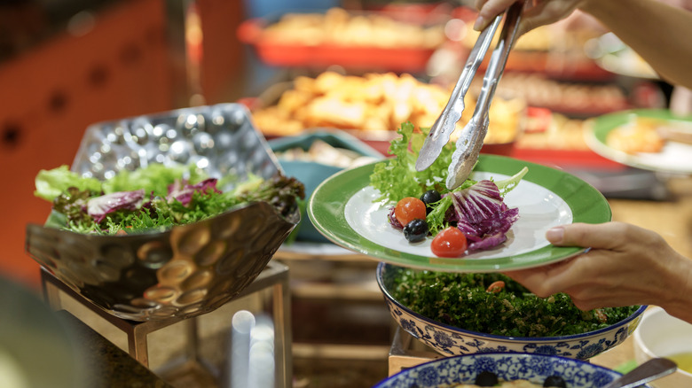 Person putting salad on plate at salad bar