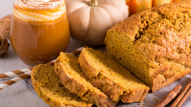 Three slices of pumpkin bread laid beside its loaf next to a pumkin spice latte