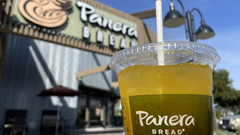 A cup of Charged Lemonade is framed in front of a Panera Bread restaurant