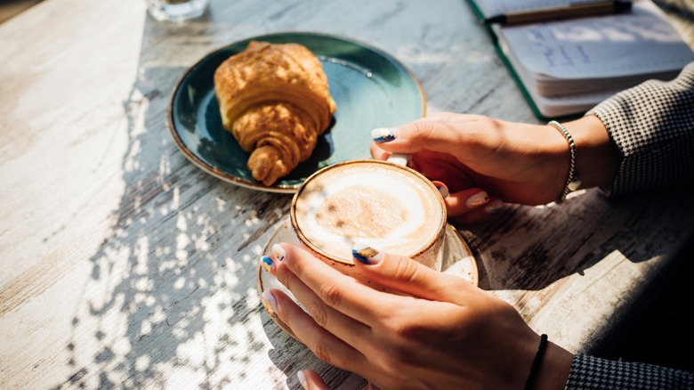 A cappuccino and a croissant at a wooden picnic table