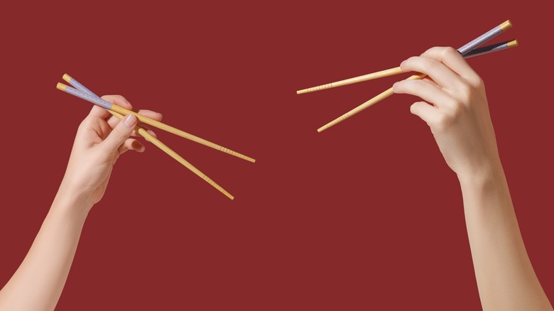 Two hands holding up chopsticks