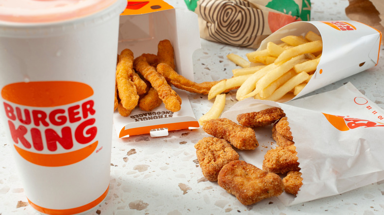 A Burger King meal with chicken fingers and nuggets, a drink, and fries on a speckled table