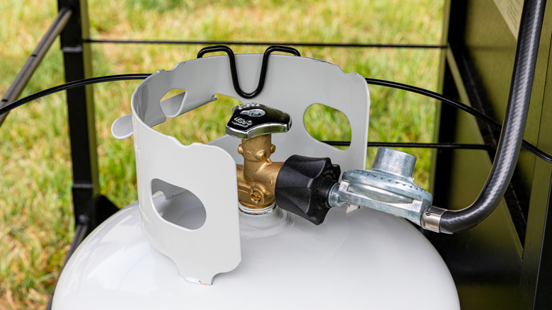 Close up of a propane tank beneath a grill with a hose connected to it