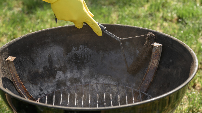 A person cleans a grill firebox that's been covered with ash