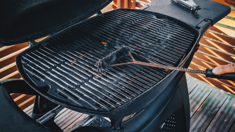 A person cleaning a used black grill with a long wire brush