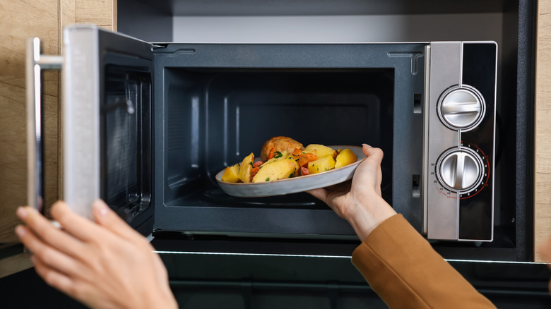 A hand putting a plate of food inside a microwave