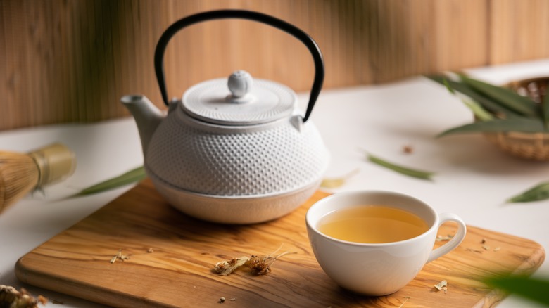 Green tea in a cup next to a teapot on a wooden chopping board