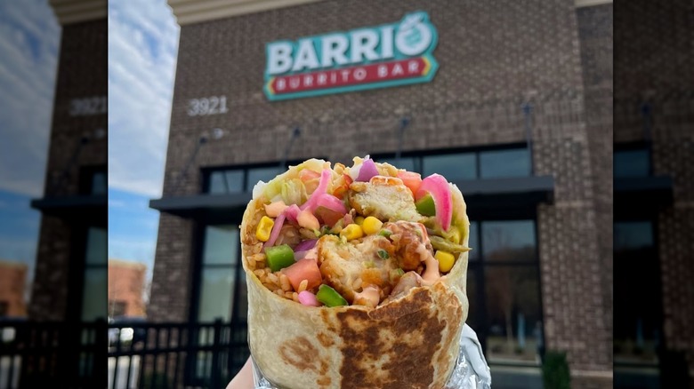 Close-up of burrito with unfocused Barrio Burrito Bar store and sign in the background