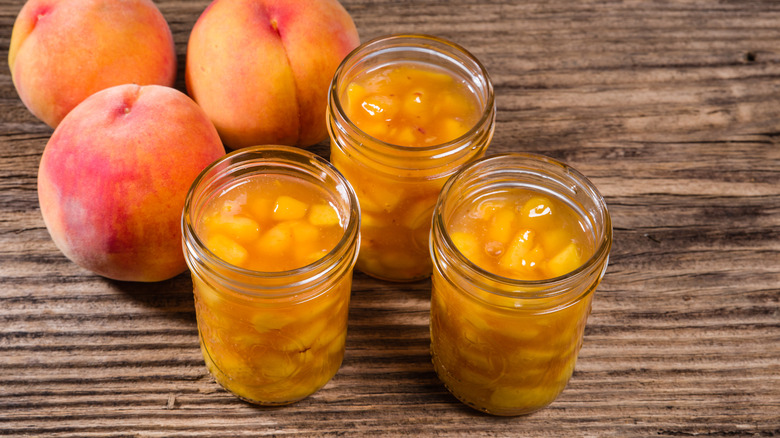 Jars of homemade peach pie filling next to peaches on a table