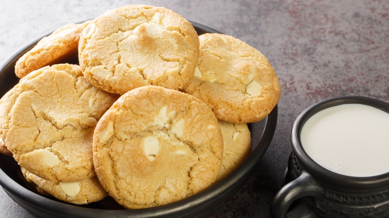 bowl of white chocolate macadamia nut cookies next to a mug of milk