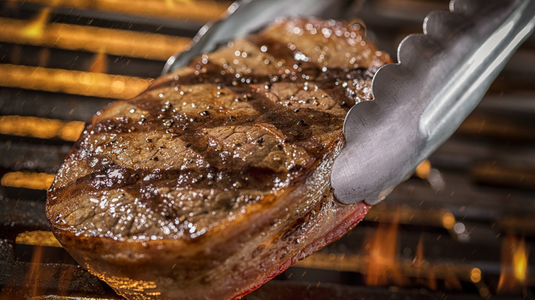 Tongs holding grilled filet mignon