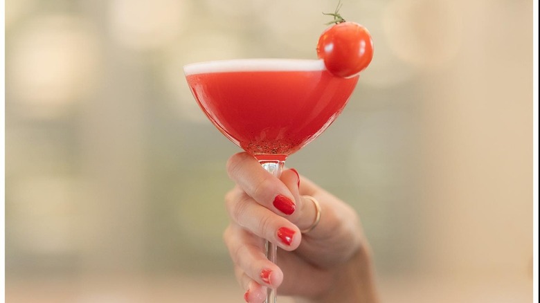 Red drink in coupe glass with tomato garnish