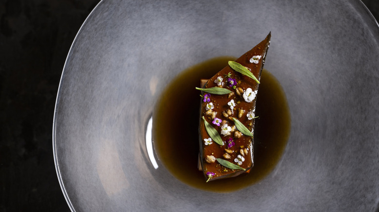 Artfully presented steak with jus, decorated with flowers, served at Atomix restaurant.