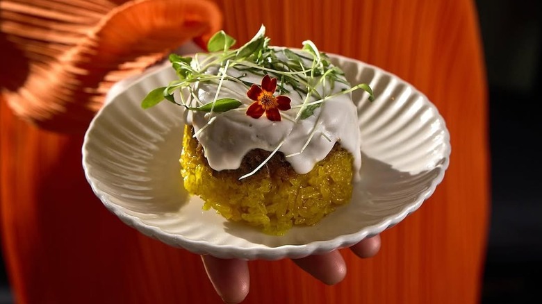 Hand holding a dish of golden turmeric rice with coconut cream