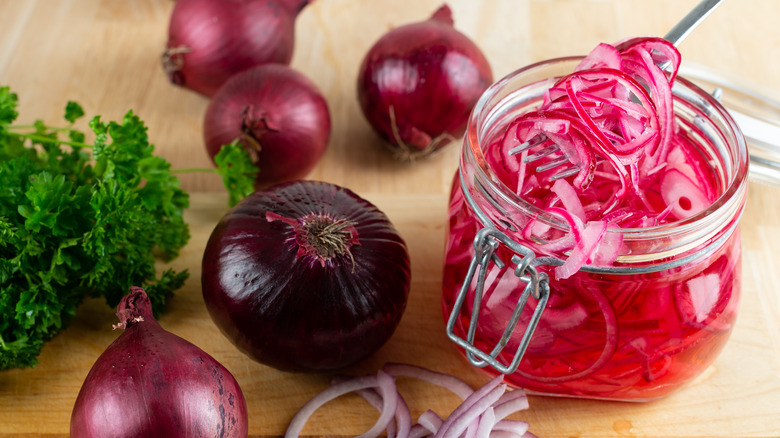Pickled red onion in jar surrounded by raw red onions