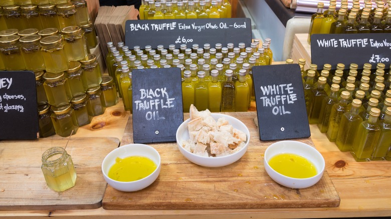 Black and white truffle oil in small white bowls on wooden cutting board with bread nearby to dip and black signs with white writing and small bottles of oil on a wooden table.