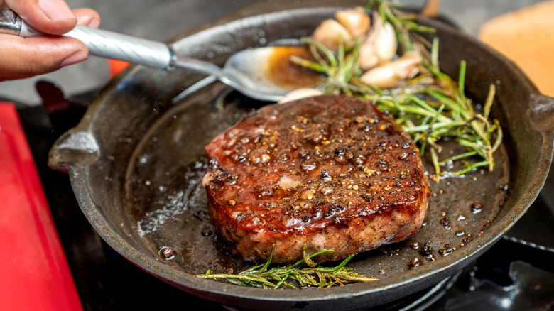 A steak cooking in a cast-iron pan with herbs and garlic