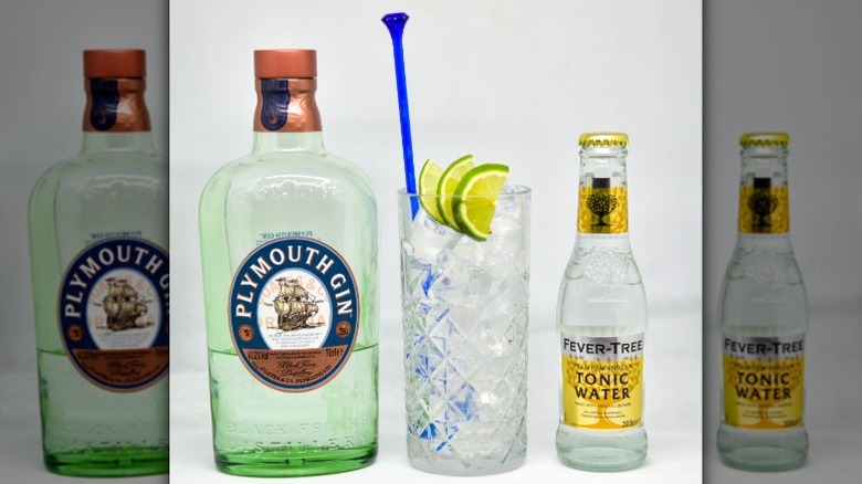 A bottle of Plymouth gin next to a cup of ice with limes and a bottle of Fever Tree tonic water