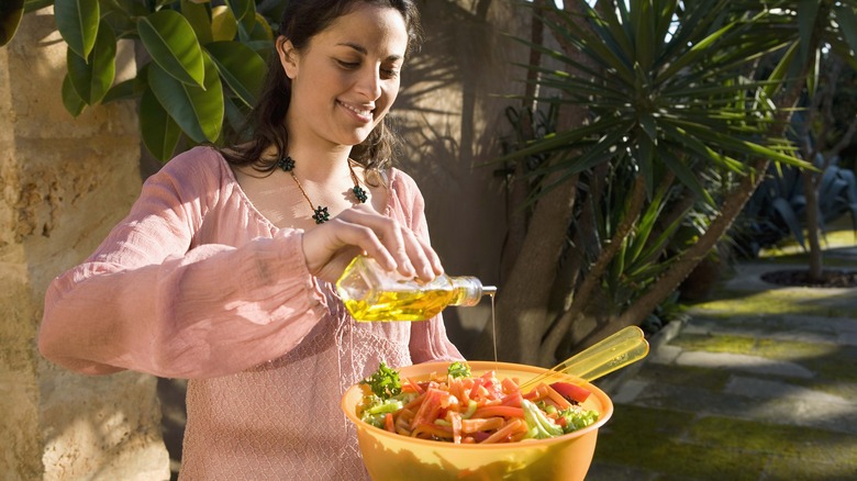 Woman pouring oil on salad