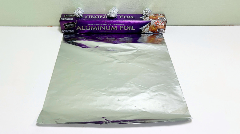 A box of Signature Select Aluminum Foil next to a sheet and some balls of aluminum foil