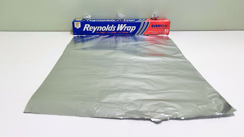 A box of Reynolds Wrap Aluminum Foil next to a sheet and some balls of aluminum foil