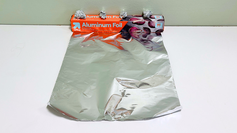 A box of up and up Aluminum Foil next to a sheet and some balls of aluminum foil