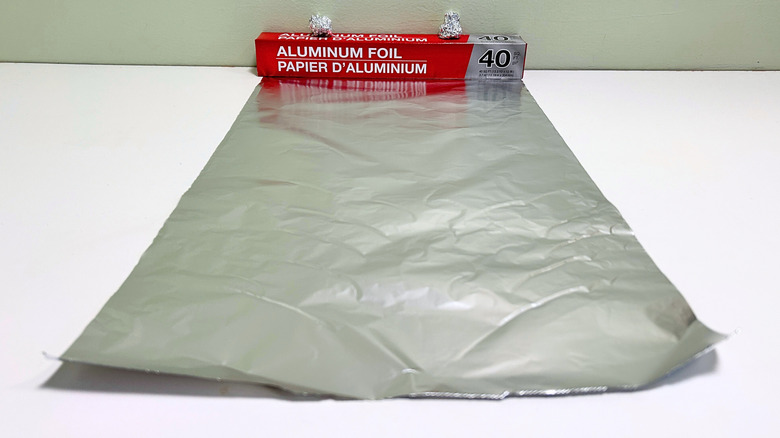 A box of Dollar Tree Aluminum Foil next to a sheet and some balls of aluminum foil