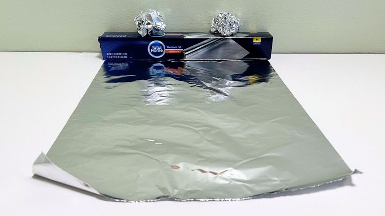 A box of Total Home Aluminum Foil next to a sheet and some balls of aluminum foil