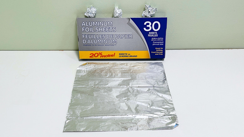 A box of Dollar Tree Aluminum Foil Sheets next to a sheet and some balls of aluminum foil