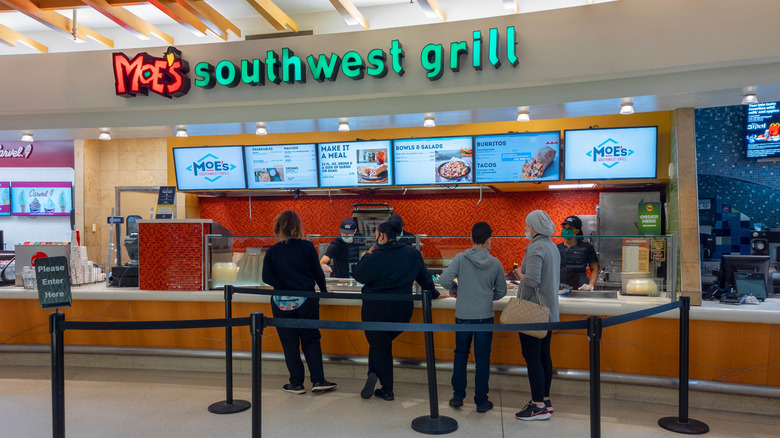 Customers standing in line at a Moe's in a food court.