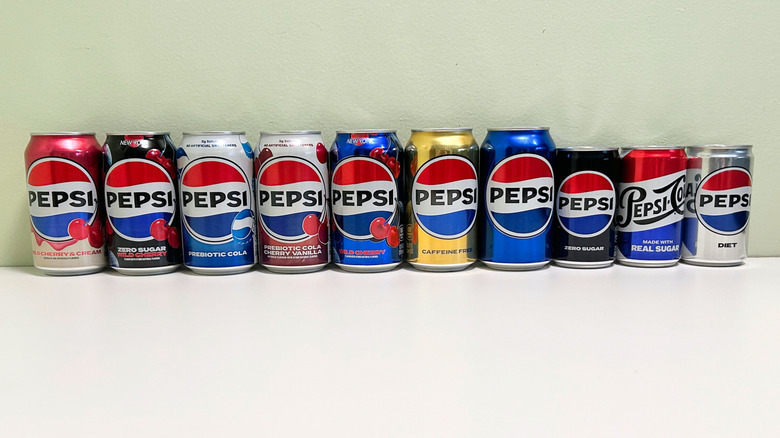 Ten cans of Pepsi are lined up against a wall