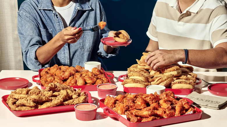 two people making plates from an array of Zaxby's products including tenders, wings, boneless wings, and chicken sandwiches