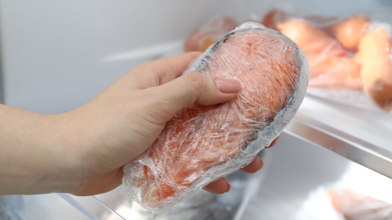 Woman holding frozen salmon steak wrapped in plastic