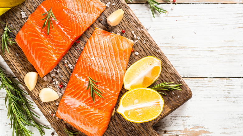 Salmon filets on cutting board surrounded by garlic, lemon, salt and herbs