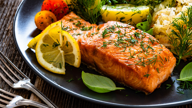 Cooked salmon filet on plate with lemon slices and other sides
