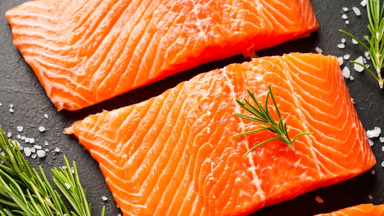 Two raw salmon filets with flakes of salt and herbs on the side