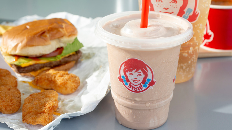 Wendy's Frosty in the forefront with a cheeseburger and chicken nuggets on a white table.