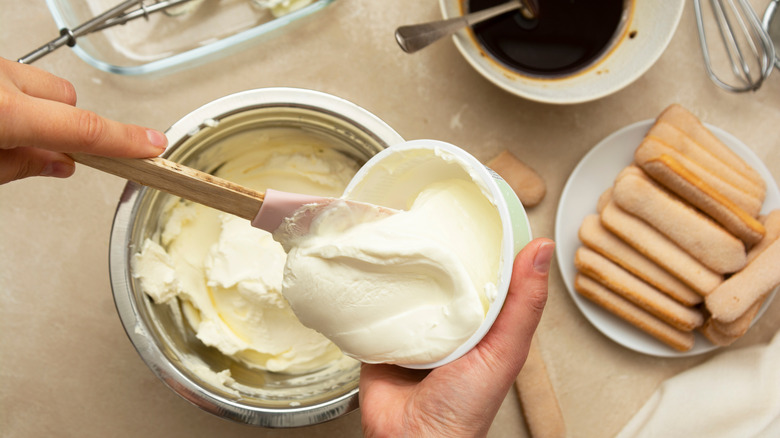 Spooning cream into a bowl surrounded by baking ingredients